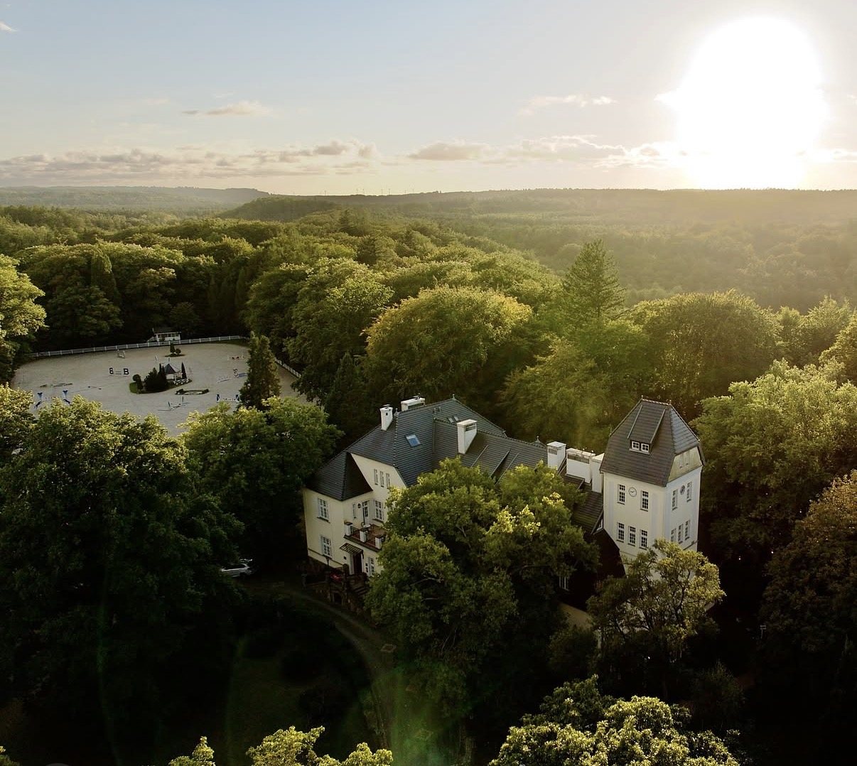 Pałac Ciekocinko from above at sunset, surrounded by forest, with the riding arena beside it