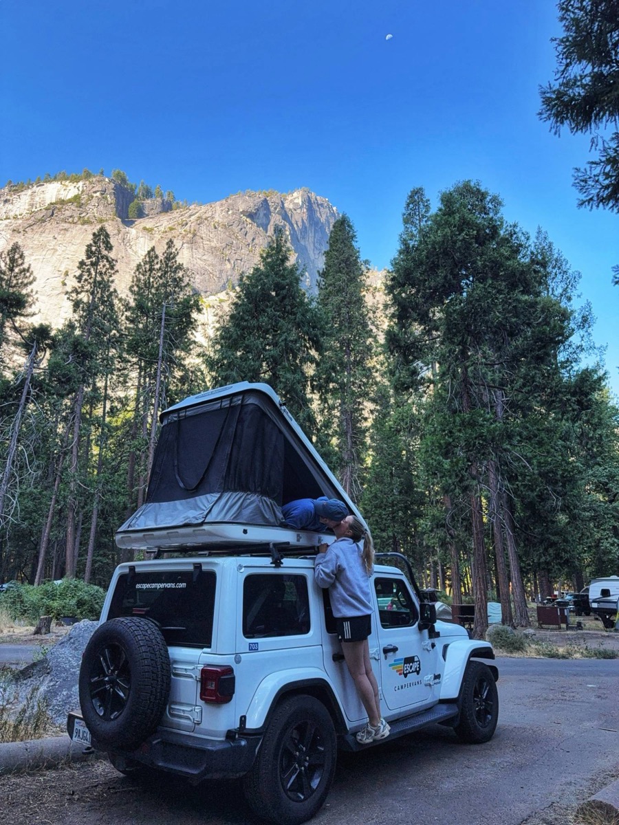 A kiss over the roof tent of a camper jeep beneath granite cliffs